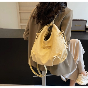 Détail de la texture en cuir PU froissé jaune crème et du nœud décoratif sur le sac bandoulière