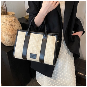 Detailed view of beige woven tote bag with black leather straps on a side-held model