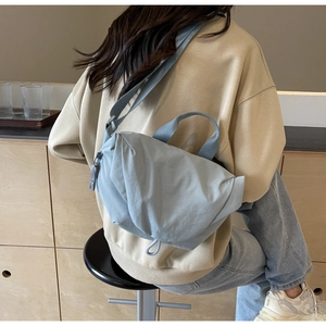 Rear view of a light blue nylon crossbody bag with drawstring detail and adjustable strap