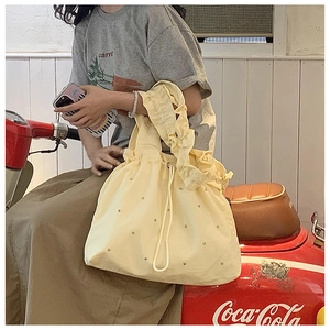 Detail of yellow canvas tote bag featuring pleated handles and decorative metal studs