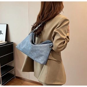 Blue denim texture hobo bag with metal chain strap worn on a beige blazer