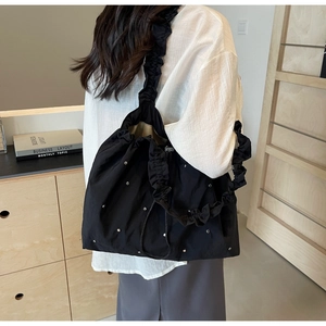 Detailed view of black ruched tote bag with silver studs on a shoulder model