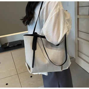 Close-up of cream canvas tote bag with black leather straps on a model in a minimal setting