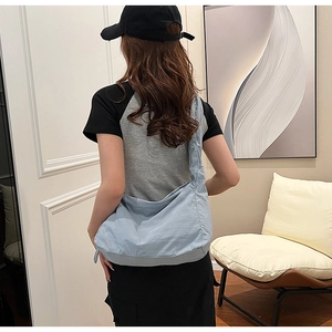 Close-up of a light blue nylon hobo bag worn by a model in a minimalist home interior