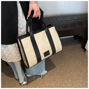 Detail of a rectangular straw woven tote bag with black leather trim and embossed logo tag