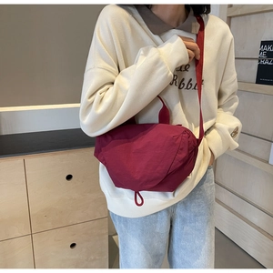 Burgundy nylon crossbody bag featuring drawcord detailing worn by a model in a casual style