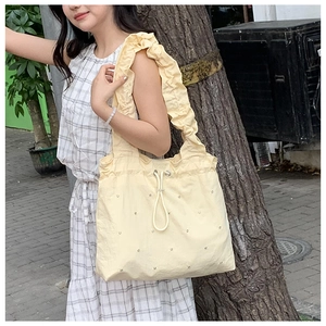 Detail of light yellow nylon tote bag featuring rhinestone accents and wavy pleated straps