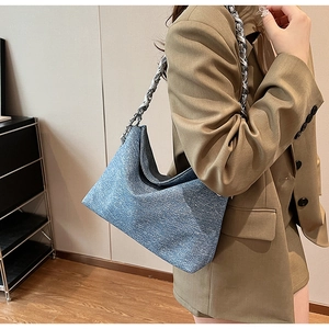 Blue textured fabric hobo bag with a thick silver chain strap on a model shoulder
