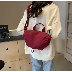 Detail of burgundy nylon crescent bag worn crossbody against a white hoodie
