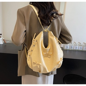 Detail of light yellow pleated tote bag with bow accent shown on model in a cafe