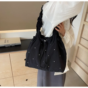 Detail of black drawstring shoulder bag featuring silver studs and ruffled strap design