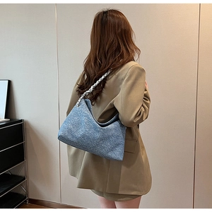 Detail of blue denim texture crossbody bag with silver woven metal chain strap on model