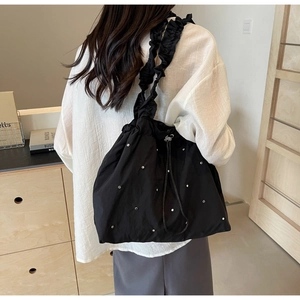Detail of black nylon tote bag with ruffle shoulder strap and silver stud accents