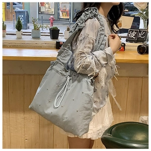 Detail of blue-grey nylon tote bag with silver studs and ruffled shoulder strap