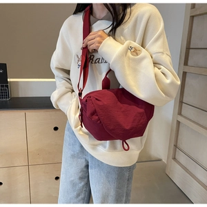 Detail of dark red nylon crossbody bag with adjustable strap shown on model outdoors