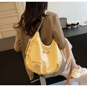 Detail of a creamy yellow tote bag with ribbon bows and pleated leather texture