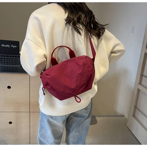 Close-up of a burgundy nylon crossbody bag with pleated texture worn by a model