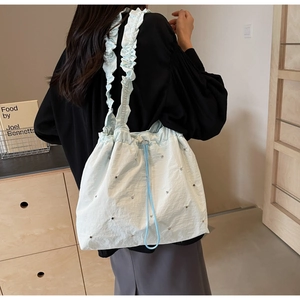 Detail of mint blue drawstring tote bag featuring ruffled shoulder straps and metal studs