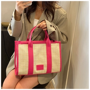 Detail of woven straw tote bag with rose pink leather trim and textured top handle
