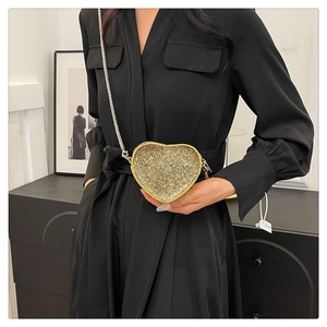 Detail of a golden heart-shaped rhinestone handbag with a thin metal chain on a model