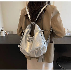 Détail d'un sac à dos argenté métallisé avec des nœuds décoratifs et texture froissée