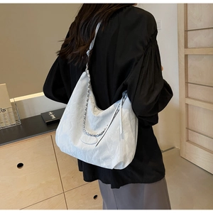 Detail of minimalist cream hobo bag with silver chain strap on model in modern interior