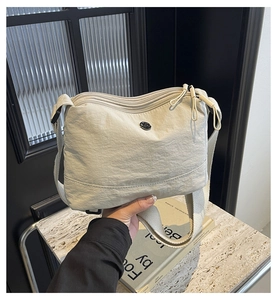 Detail of light beige pleated nylon crossbody bag showing three zippers and textured strap