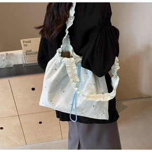 Detail of light blue ruffled tote bag with silver studs and nylon texture shown on model