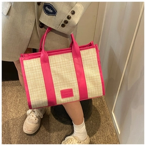 Detail of a beige woven tote bag with peach pink leather trim and handles held by a model