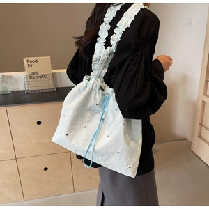 Detail of light blue pleated shoulder bag with silver rivets and ruffled strap on a model