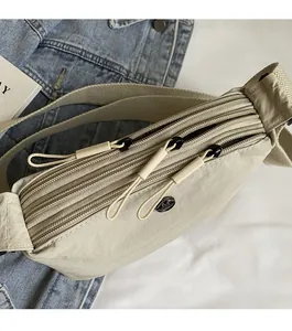 Detail view of the multi-layer smooth zippers on a beige nylon crossbody bag