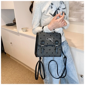 Detail of grey PU handbag with black polka dots and silver bow decoration worn by a model