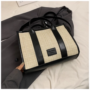 Straw weave tote bag with black leather trim and dual straps on casual blazer background