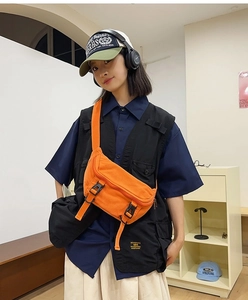 Close-up of bright orange canvas crossbody bag with black buckles on a female model