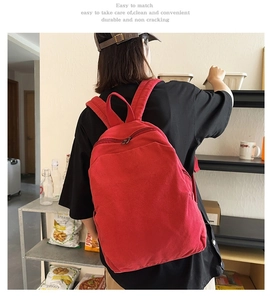 Detail of red canvas backpack with adjustable straps worn by a model in a cozy setting