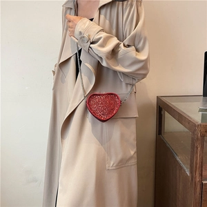 Detail of red heart-shaped rhinestone handbag worn with a classic khaki trench coat