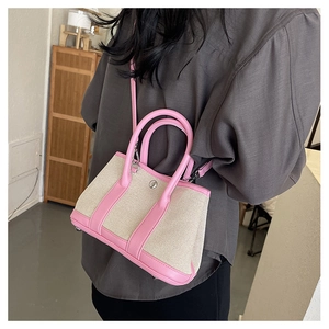 Close-up of beige canvas handbag with pink leather trim and metal protective feet