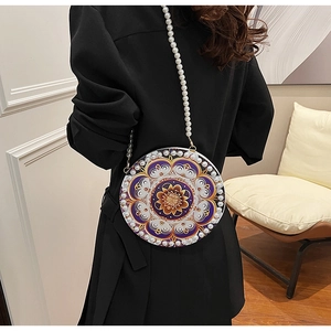 Detail of round crossbody bag featuring purple floral patterns and white pearl strap