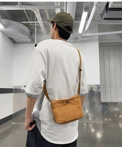 Detailed back view of a brown canvas crossbody bag worn by a male model in a corridor