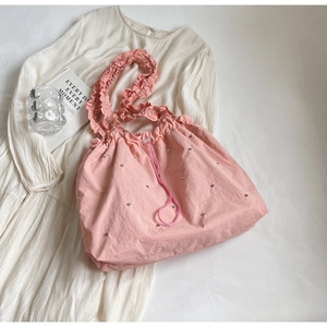Pink ruffled tote bag with silver studs and drawstring closure on white dress background