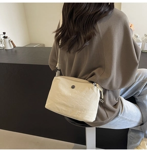 Close-up of beige nylon crescent bag featuring a circular metal logo and zip closure