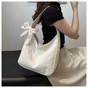 Close-up of beige canvas shoulder bag with floral embroidery and lace bow detail