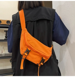 Close-up of bright orange canvas crossbody bag featuring black buckles and fabric texture