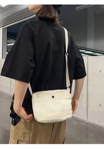 Detail of off-white canvas crossbody bag with black metal snap button and strap