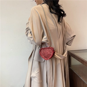Detail of a red heart-shaped sequin crossbody bag with a silver chain on a trench coat