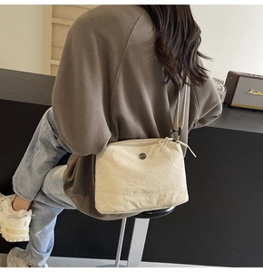 Detail of cream nylon crossbody bag with textured fabric and adjustable strap on a model