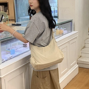 Detailed close-up of beige nylon crossbody bag with side drawstring pleated texture and strap