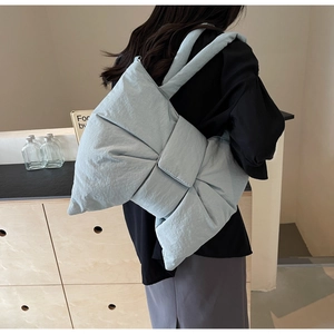 Puffy light blue bow-shaped tote bag worn by a model in a minimalist interior setting