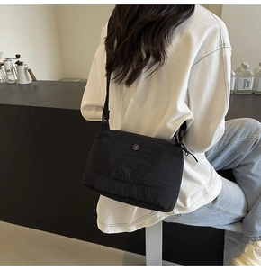 Close-up of minimalist black nylon crossbody bag with circular logo on a model