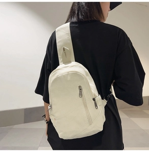 Detail view of cream canvas crossbody bag showing zippers and adjustable shoulder strap